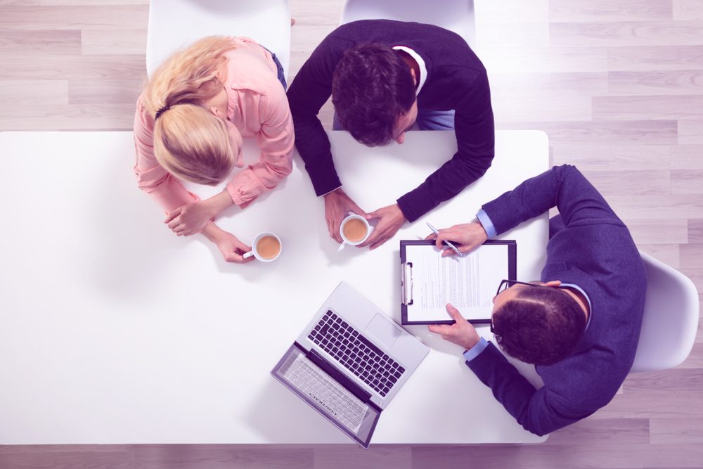 Young couple consulting male debt counseling expert with coffee cups at office desk.