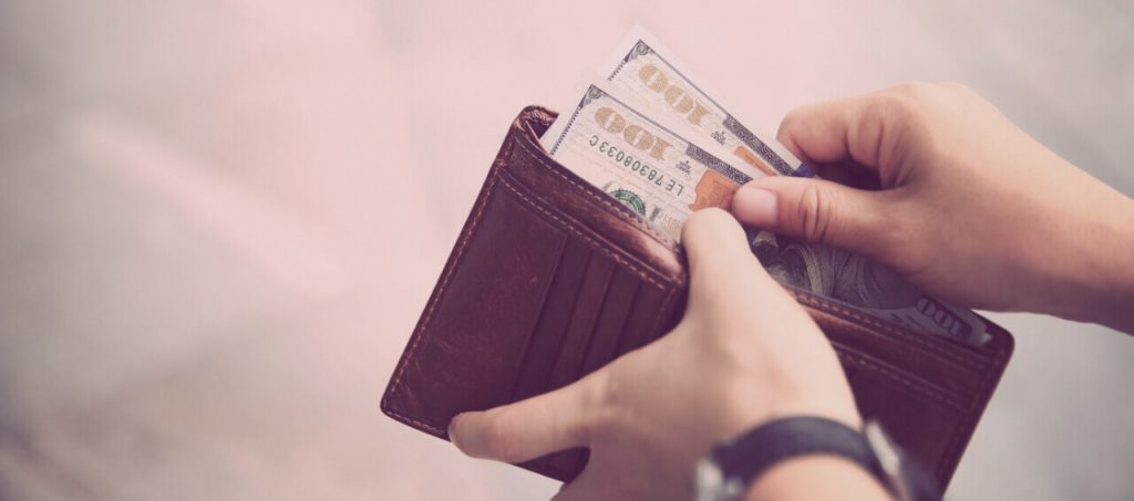 Hands taking out money from wallet on street.